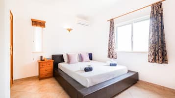 Un dormitorio con cama, mesita de noche, cómoda, ventana con cortinas y un equipo de aire acondicionado.