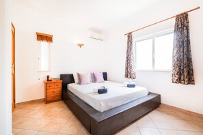 A bedroom with a bed, a nightstand, a dresser, a window with curtains, and an air conditioning unit. - Villa Los Angeles (Loulé)