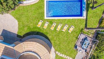 Vista aérea de una propiedad con piscina, sillas de descanso, zona de estar cubierta al aire libre y terraza de madera circular.