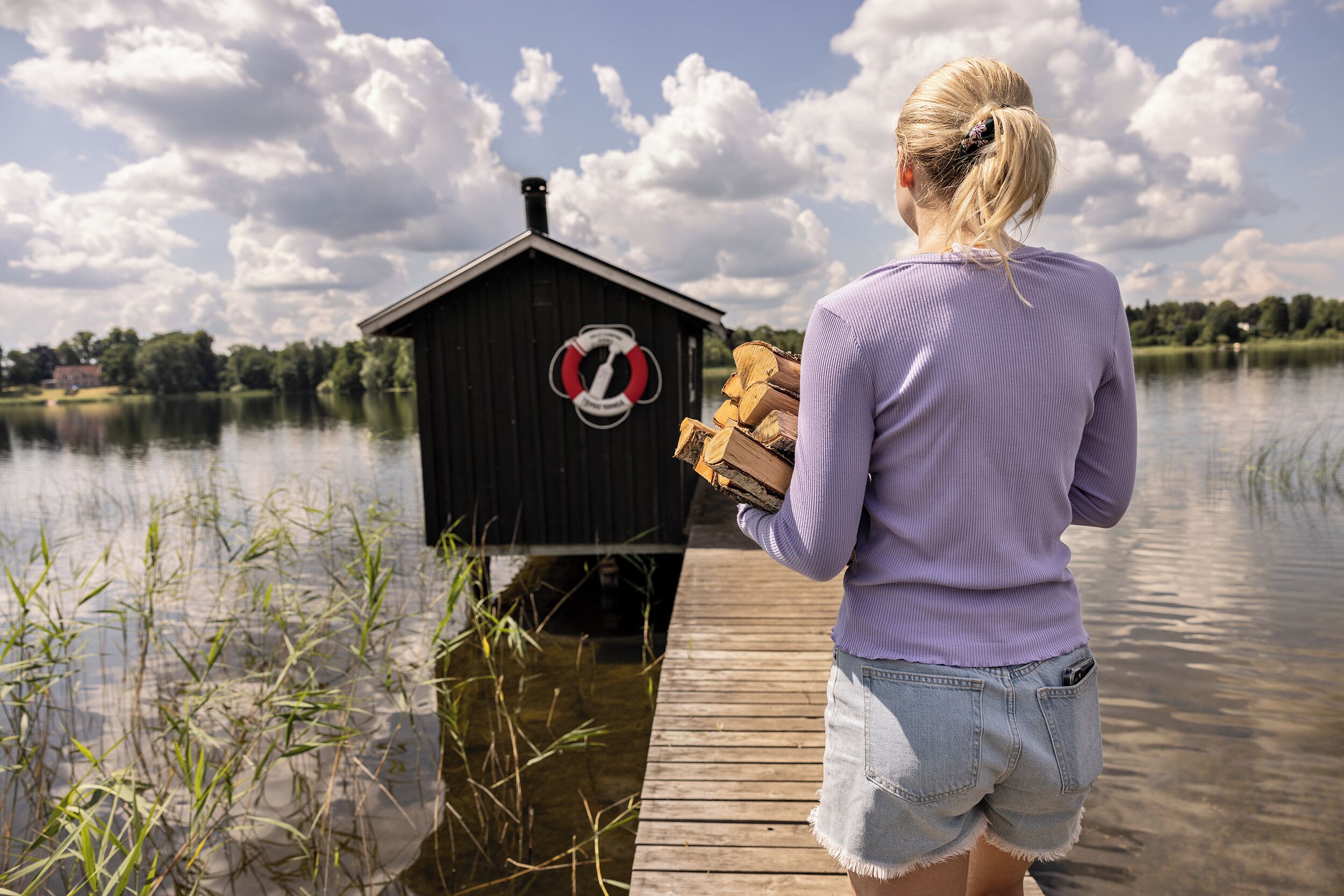 A wooden dock extending into a calm lake with a small wooden structure featuring a lifebuoy symbol.