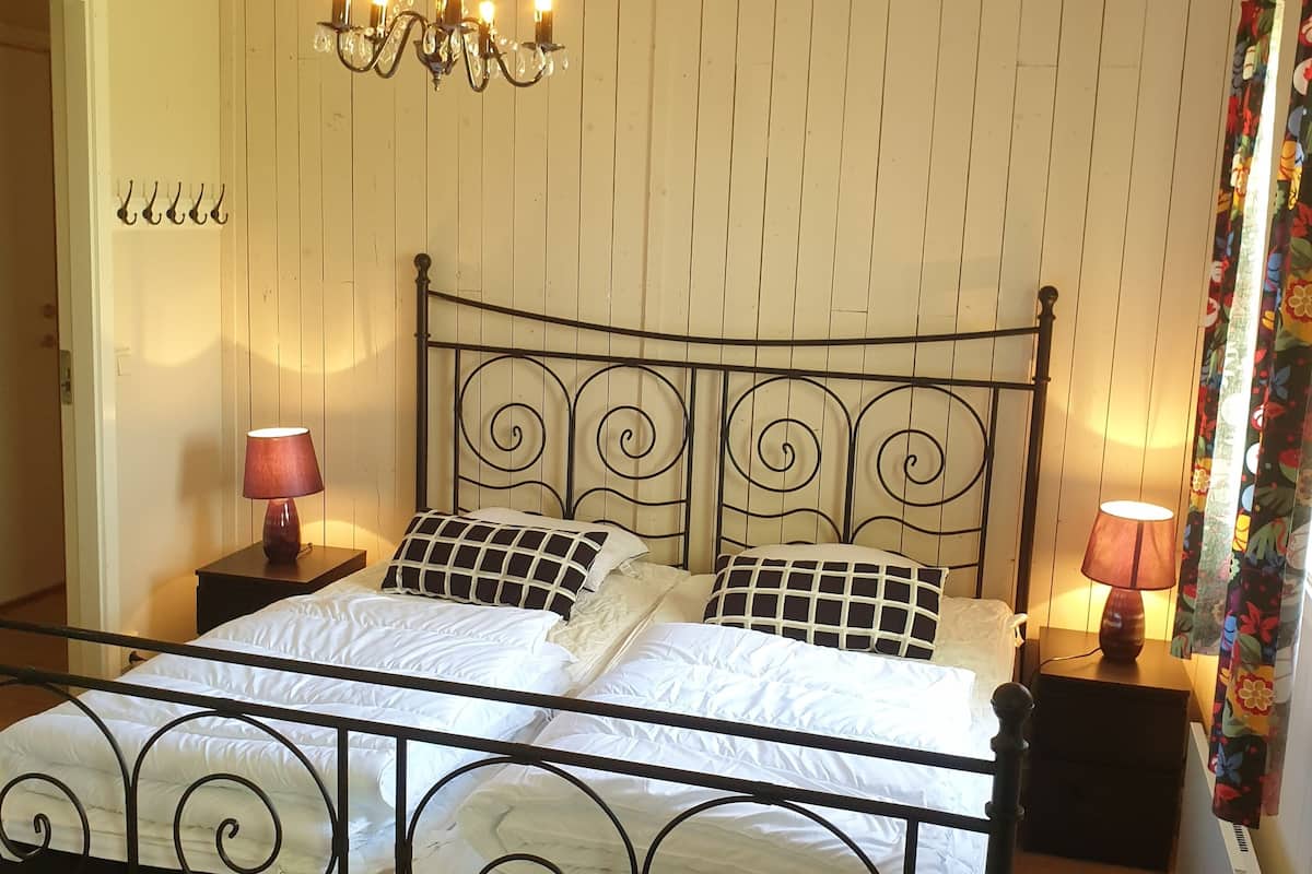 Una cama con estructura metálica, dos mesitas de noche con lámparas, una araña y un cabecero de madera con una puerta.