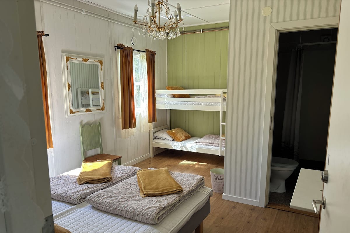 Una habitación con literas, suelo de madera, un candelabro y una puerta que da al baño.