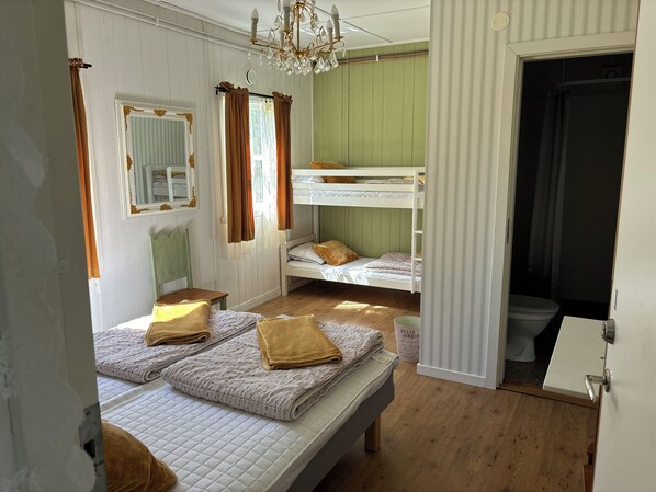 A room with bunk beds, a wooden floor, a chandelier, and a door leading to a bathroom. - Valle camping (Axvall)