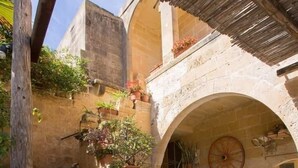 Un patio con escalones de piedra que conducen a una puerta, rodeado de plantas en macetas y un techo de paja rústico.