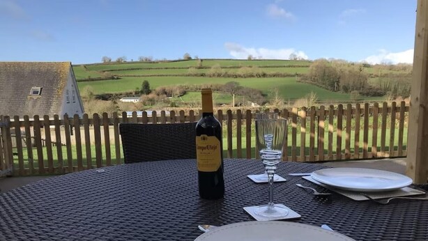 A table set outdoors with a bottle of wine, a glass, and plates, overlooking a rural landscape. - The Stables - Stokeinteignhead (Torquay)