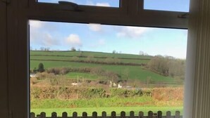A window with a view of a rural landscape, including fields, a fence, and distant hills. - The Stables - Stokeinteignhead (Torquay)