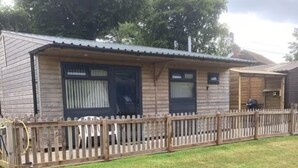 A single-story wooden building with a fenced yard, a covered porch, and a small attached structure. - The Stables - Stokeinteignhead (Torquay)