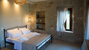Ein Schlafzimmer mit einer Steinsandsteinwand, einem Bett mit weißen Leinentüchern, einer Pendelleuchte und einem Fenster mit Vorhängen.