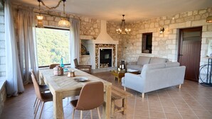 Ein geräumiger Wohnbereich mit Kamin aus Stein, einer Couch und einem Esstisch mit Stühlen.