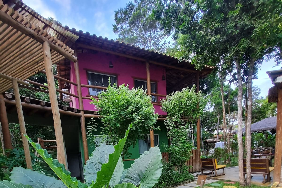 Un jardín con pérgola, abundante vegetación y un edificio de fachada rosa.