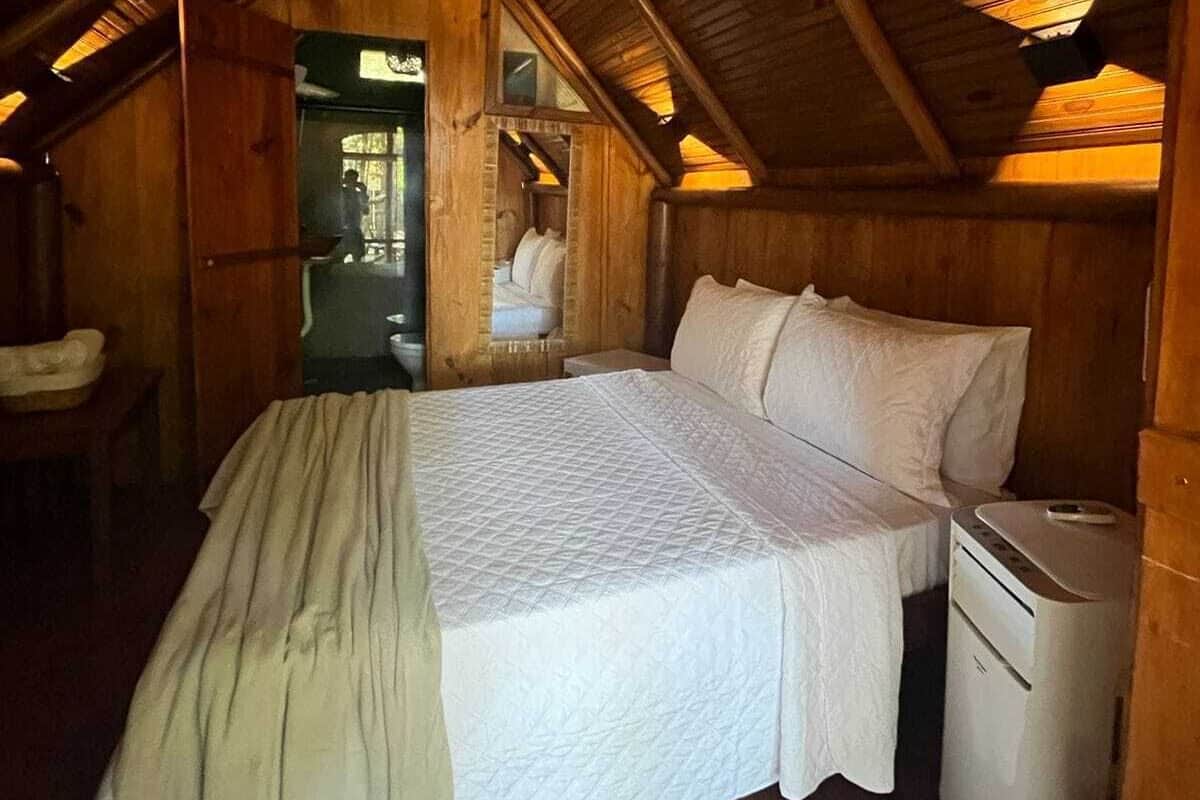 Un dormitorio acogedor en el ático, con techo de madera, una cama con ropa blanca y un pequeño calentador en el suelo.