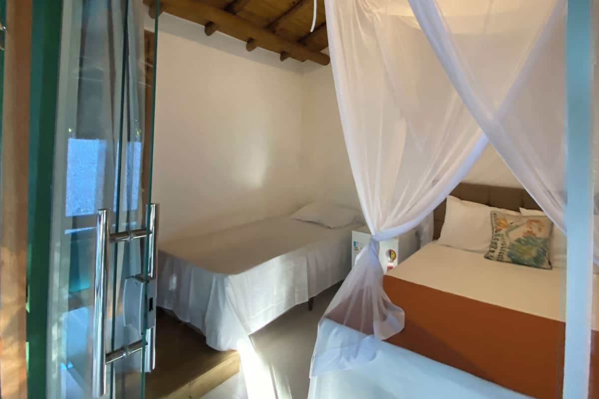 Una habitación con dos camas, una con dosel, y un ventanal que da al exterior.