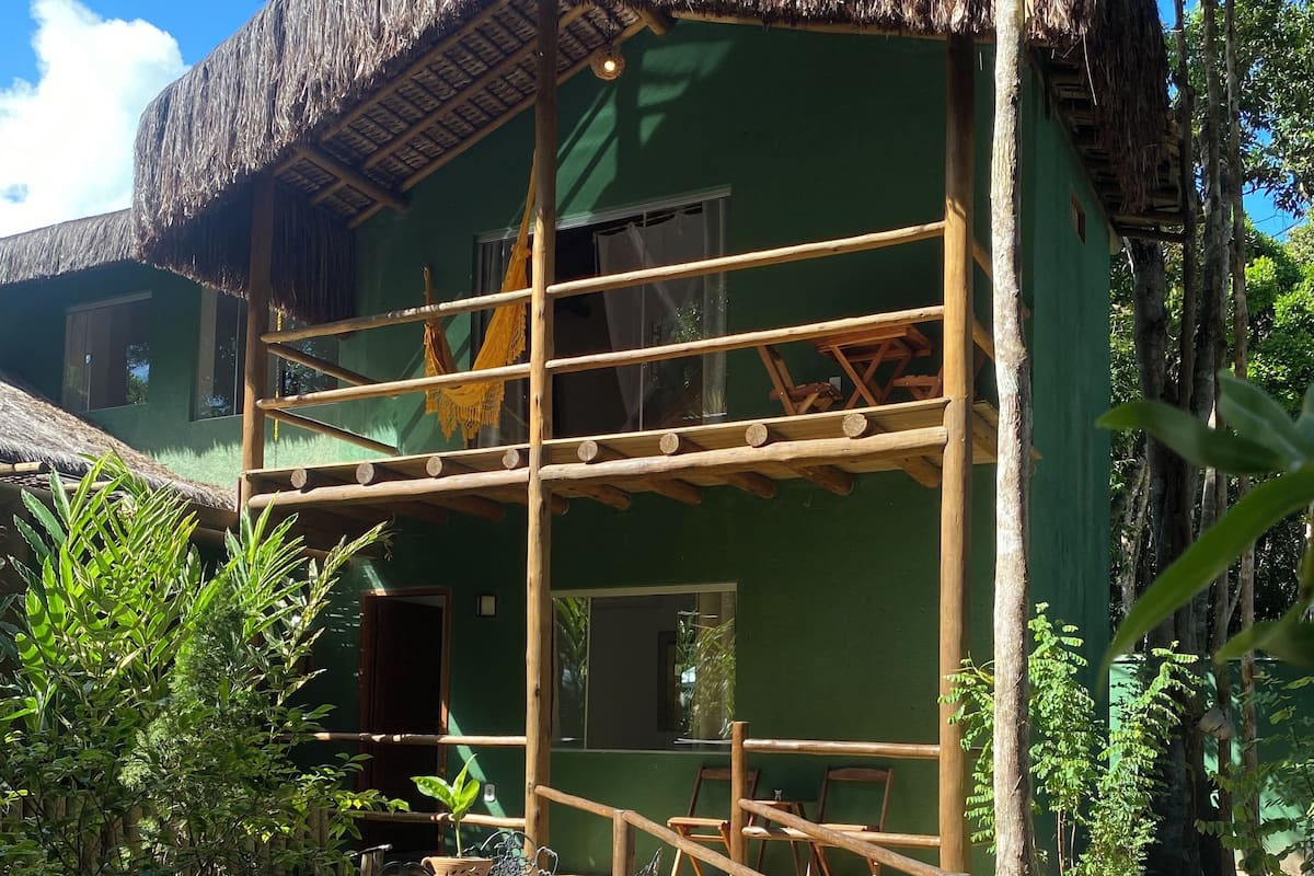 Un edificio verde con techo de paja, andamios de madera y una terraza de madera con sillas y mesas.
