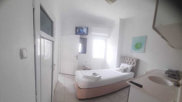 A bedroom with a bed, a small bedside table, a wall-mounted TV, and a window. - Kibar Apart Pansiyon (Kusadasi)