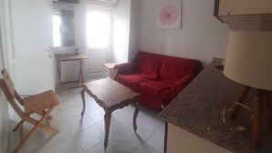 A living room with a red sofa, a wooden chair, a small table, and a lamp. - Kibar Apart Pansiyon (Kusadasi)