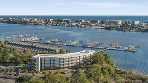 Un port de plaisance avec des bateaux amarrés, un bâtiment moderne à la façade incurvée et, au loin, une vue sur le paysage urbain côtier.