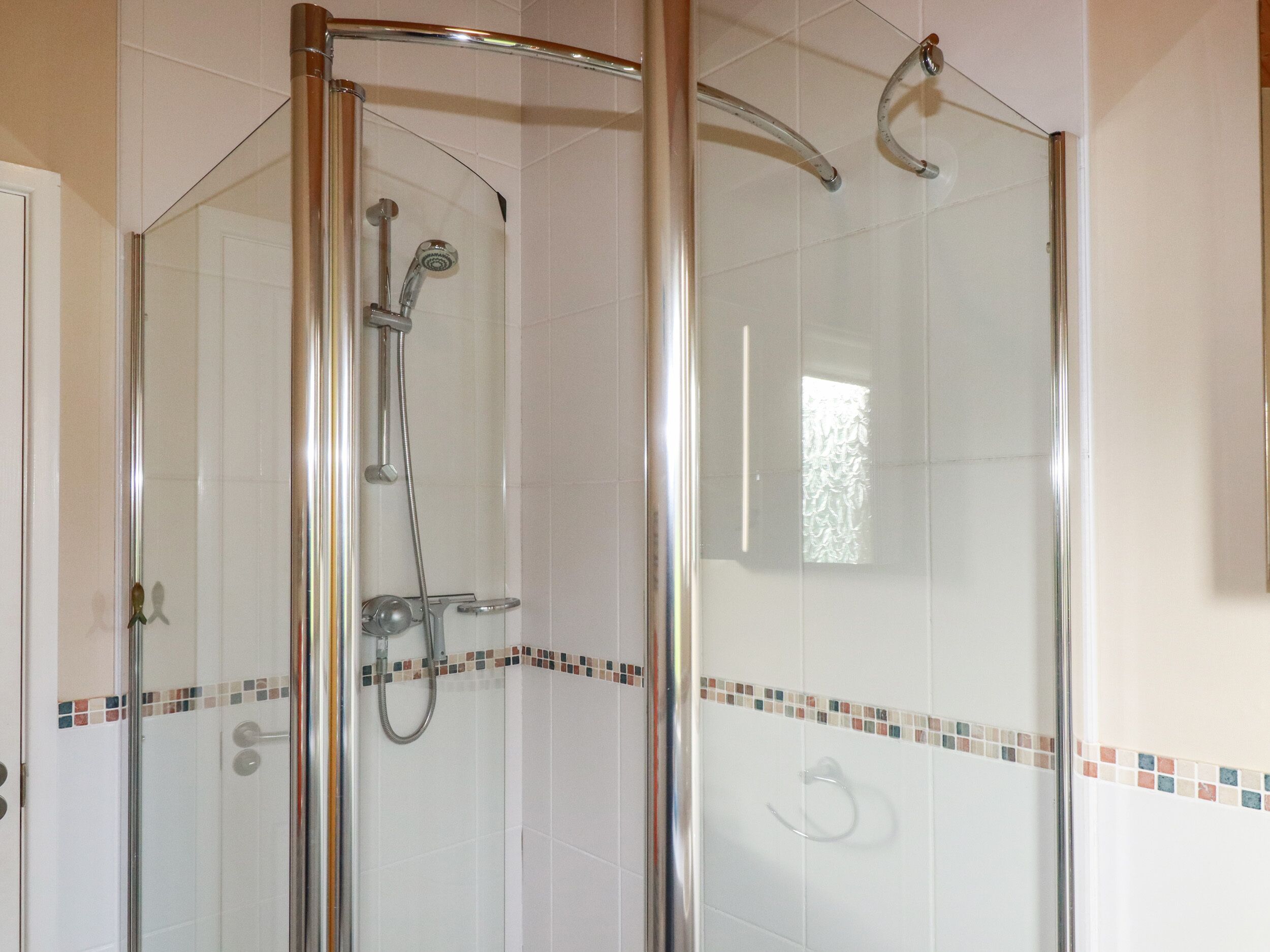 A glass-enclosed shower with a handheld showerhead and a wall-mounted faucet.