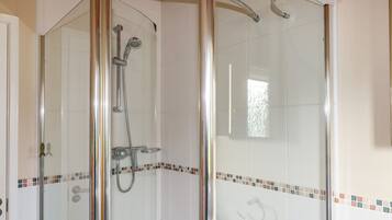 A glass-enclosed shower with a handheld showerhead and a wall-mounted faucet.