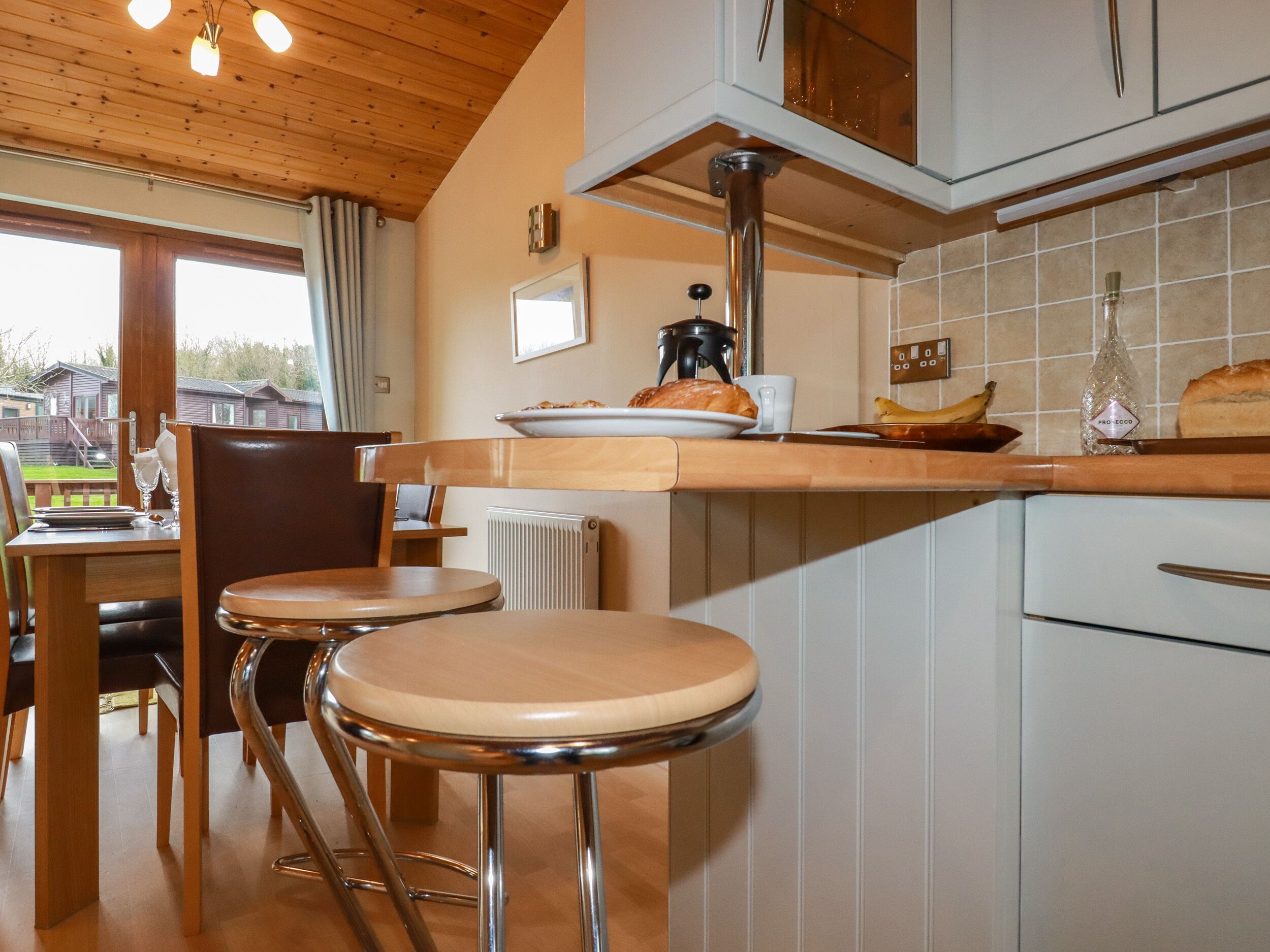 Una cucina con soffitto in legno, una zona pranzo con due sgabelli, un termosifone e una finestra con tende.