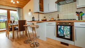 Una cocina moderna con armarios blancos, un horno de acero inoxidable y una zona de comedor de madera con dos taburetes de bar.