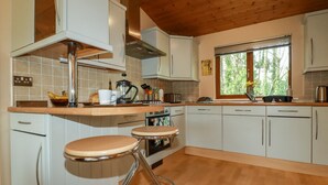 Una cocina moderna con armarios blancos, techo de madera y ventana con vista a árboles.