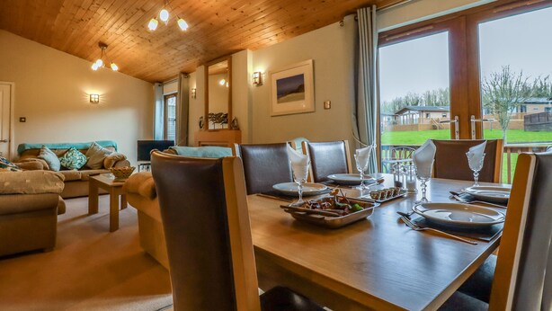 Comedor con mesa de madera preparada para cuatro personas, sofá y vistas al exterior.