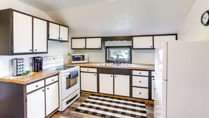 A compact kitchen with white cabinets, a microwave, a stove, and a refrigerator. - Greenwich Countryside Apartment w/ Shared Yard (Greenwich)