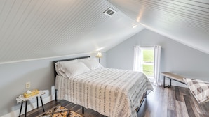 A bedroom with a sloped ceiling, a bed with patterned bedding, a bedside table with a tissue box, and a window with curtains. - Greenwich Countryside Apartment w/ Shared Yard (Greenwich)