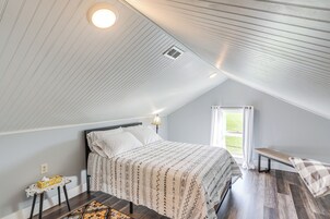 Un dormitorio con techo inclinado, una cama con ropa de cama estampada, una mesita de noche con una caja de pañuelos y una ventana con cortinas.