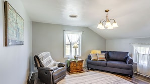 A living room with a dark leather armchair, a dark sofa with colorful cushions, a wooden cabinet, and a patterned rug. - Greenwich Countryside Apartment w/ Shared Yard (Greenwich)