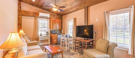 A living room with a sofa, coffee table, TV, and a kitchen area with a microwave.