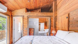 Dormitori d'una cabana de fusta amb un llit gran, un sostre de fusta i vistes a l'exterior.