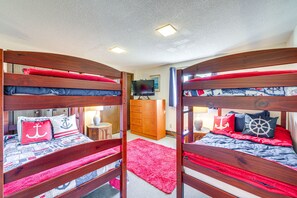 Een kamer met twee stapelbedden, een televisie, een houten dressoir en een rood vloerkleed.