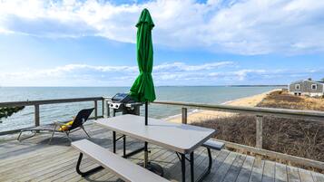 A wooden deck with a picnic table and chairs, overlooking a beach and ocean.