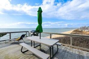 Een houten terras met een picknicktafel en stoelen, met uitzicht op een strand en de oceaan.