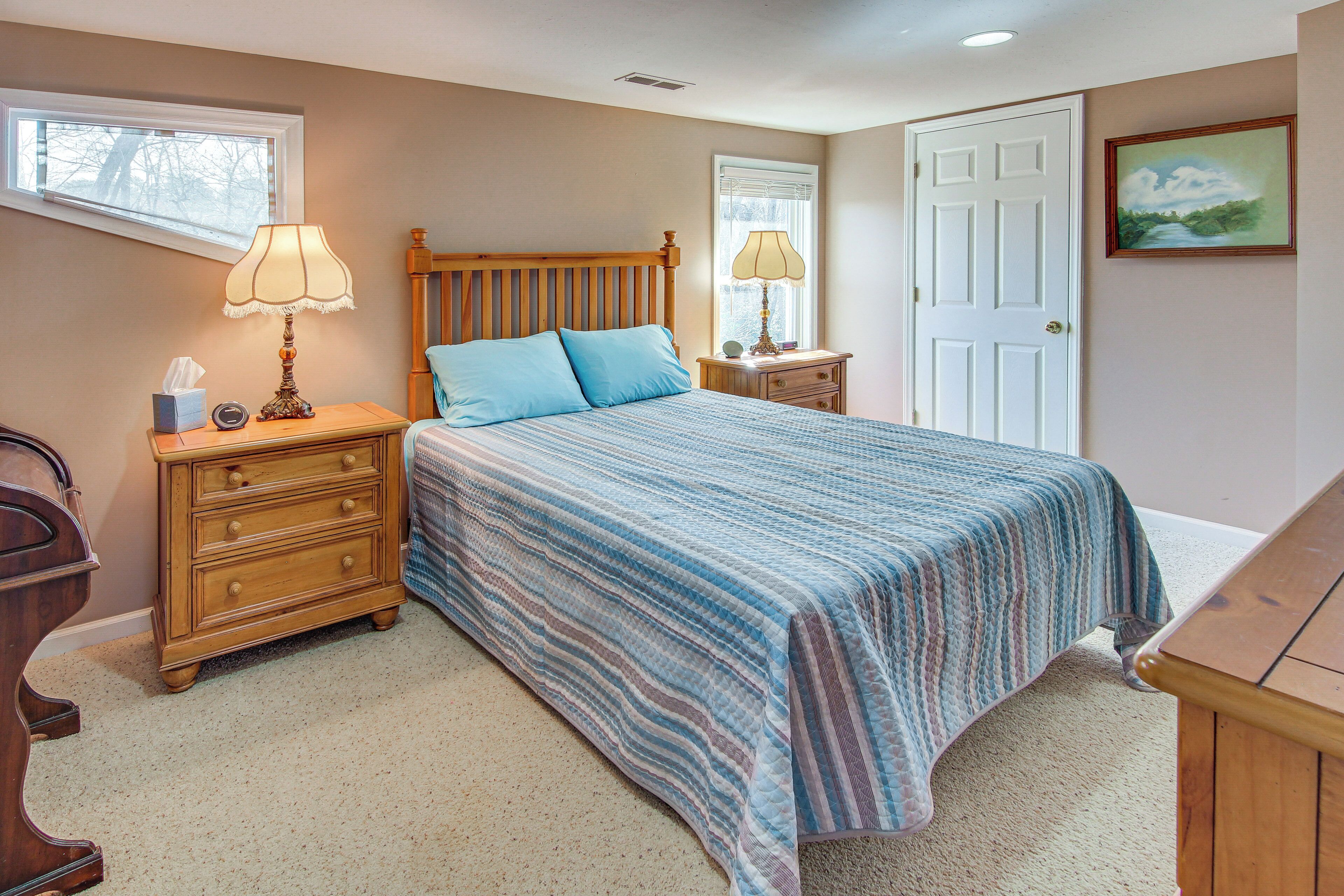A bedroom with a large bed, a nightstand with a lamp, a dresser, and a door.
