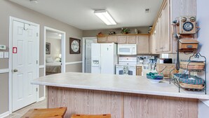 Une cuisine avec des meubles de rangement en bois, un réfrigérateur blanc, un four à micro-ondes et un tabouret de bar en bois.