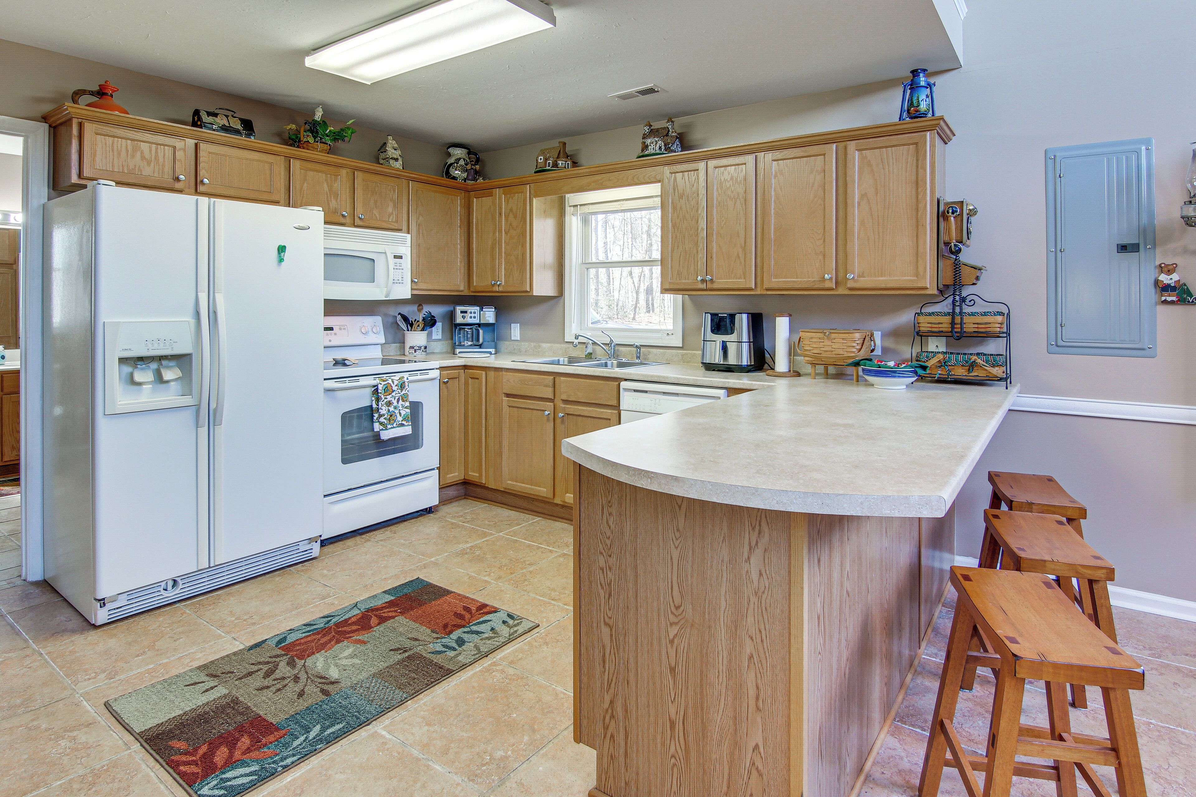 A kitchen with wooden cabinets, a refrigerator, microwave, oven, and a sink. There is a rug on the floor and wooden stools near the counter.