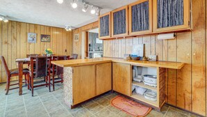 A kitchen with wooden cabinets, a countertop, and a dining area with chairs and a table. - Charming Elk Mountain Home: Hunt, Hike & Fish! (Elk Mountain)