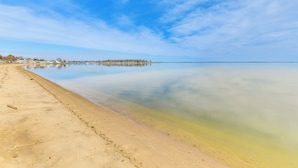 A beach with clear water, a sandy shore, and a distant shoreline with buildings. - Riverfront Colonial Beach Home w/ Private Beach! (Colonial Beach)