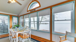 A dining area with a table and chairs, large windows with a view of a lake, and a ceiling fan. - Riverfront Colonial Beach Home w/ Private Beach! (Colonial Beach)