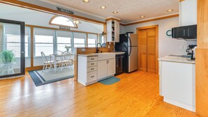 A modern kitchen with wooden cabinets, a refrigerator, and a dining area with a table and chairs. - Riverfront Colonial Beach Home w/ Private Beach! (Colonial Beach)