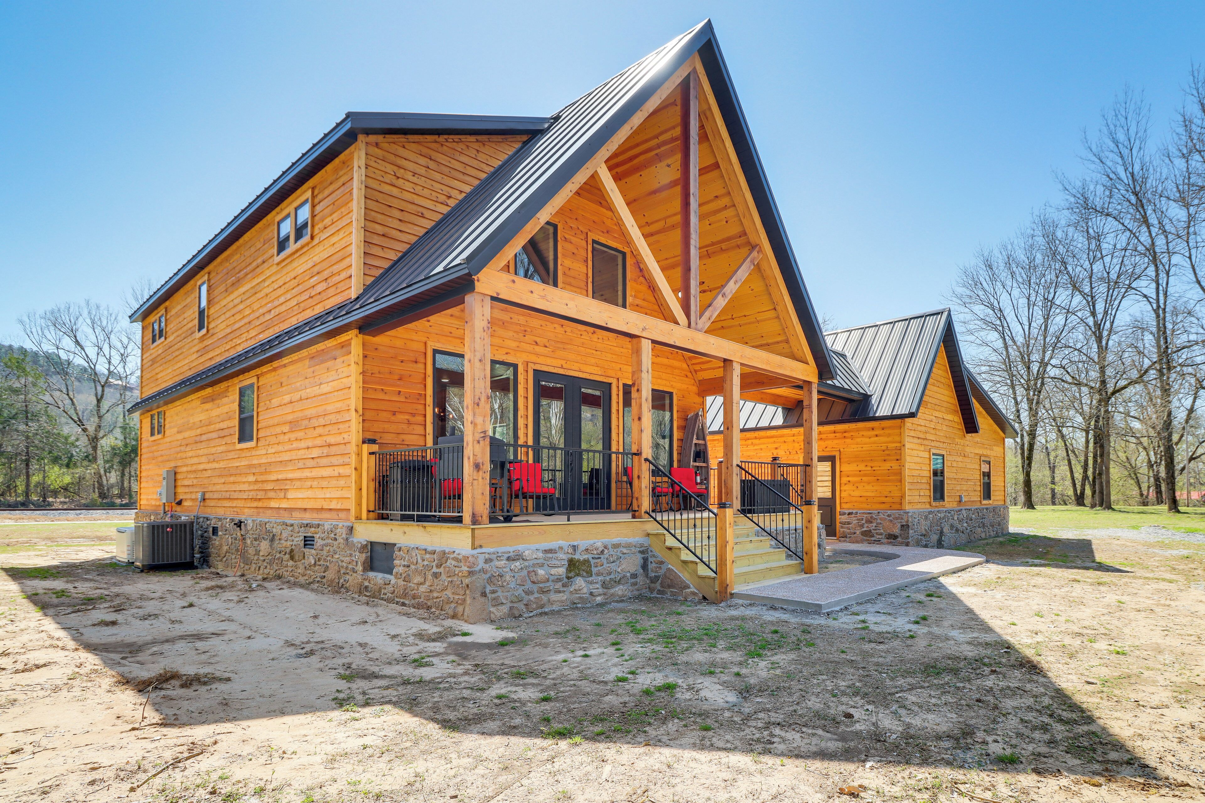 Une cabane en rondins à deux étages, avec des fondations en pierre, une véranda couverte dotée de chaises rouges et un toit en métal.