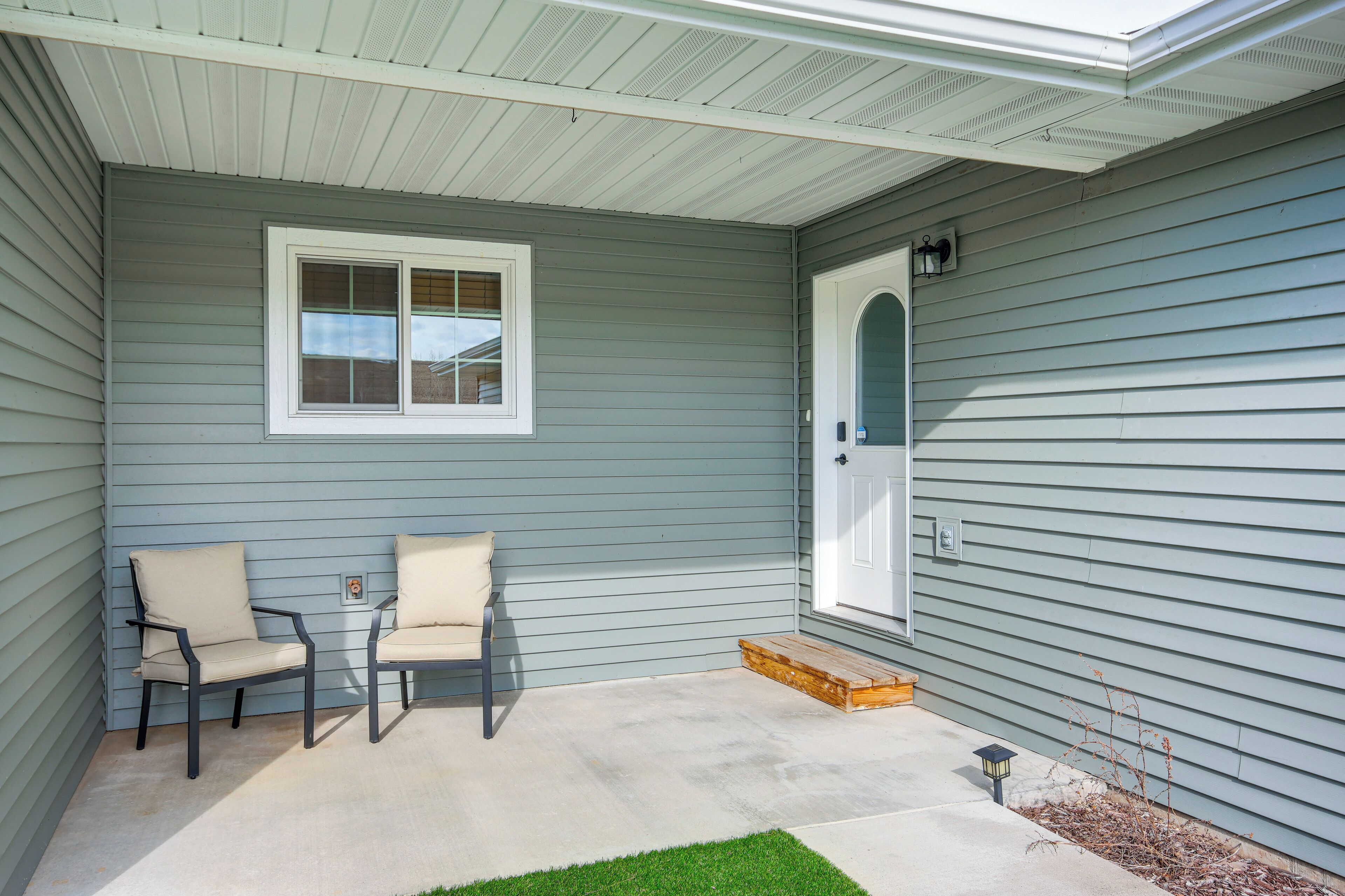 A covered porch with two chairs and a small table, a door, and a window.
