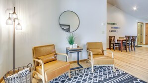 A modern living room with leather chairs, a round mirror, a small table with a plant, and a dining area in the background.