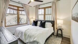 A bedroom with a bed, a ceiling fan, two windows with curtains, a bedside lamp, and a rug. - Dtwn Blowing Rock Condo w/ Private Hot Tub! (Blowing Rock)