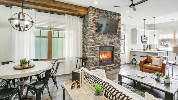 A modern living room with a stone fireplace, a dining area with a round table, and a cozy seating area with a sofa and coffee table. - Dtwn Blowing Rock Condo w/ Private Hot Tub! (Blowing Rock)
