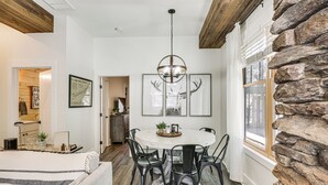 A dining area with a round table, black chairs, a chandelier, and framed artwork on the wall. - Dtwn Blowing Rock Condo w/ Private Hot Tub! (Blowing Rock)