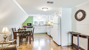 A kitchen with white cabinets, a dining table with chairs, a refrigerator, and a clock on the wall.