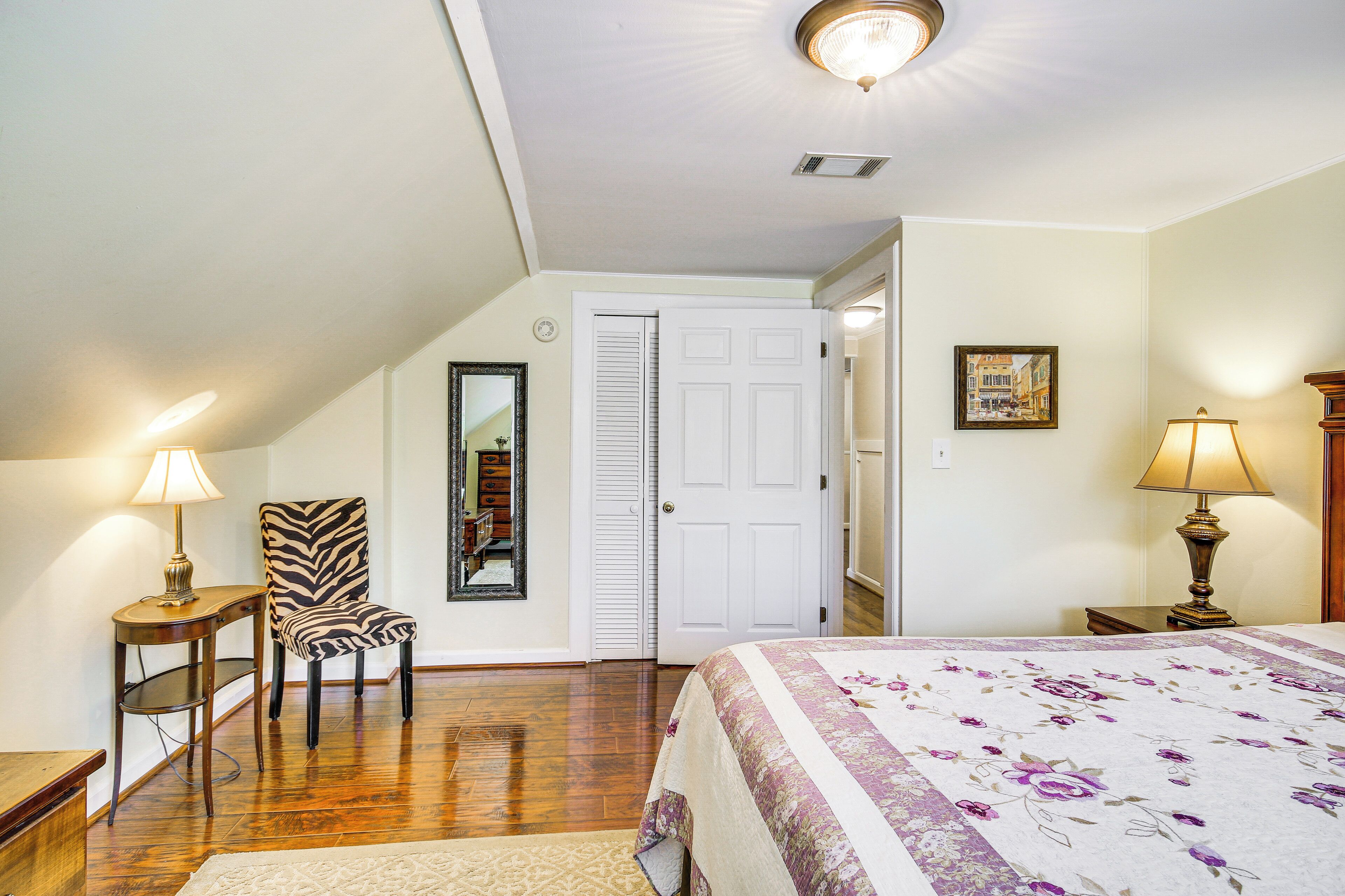 A bedroom with a bed, a zebra-patterned chair, a white door, and a lamp on a bedside table.